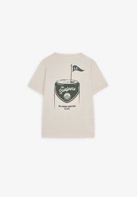 Tricou crem cu mânecă scurtă, prezentând un grafic verde închis al unei căni de golf cu un steag și textul "The Scalp" și "Competiția Regională de Golf."