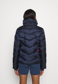 Námořnicky modrá zateplená prošívaná bunda s vysokým límcem, která má texturovaný povrch a vzor "FIRE". Obsahuje boční kapsu a kontrastní detaily.