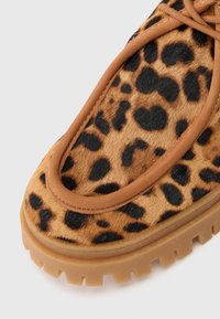 Fottøy med leopardmønster laget av teksturert pels, med en beige lærdetalj og en chunky, kontrasterende gummisåle med zigzag-mønster.