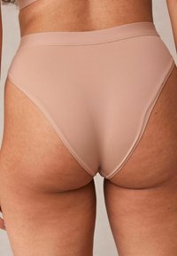 Culottes beiges taille haute en tissu lisse et extensible. Dotées de coutures minimales et d'un design sans coutures pour plus de confort et une silhouette épurée.