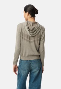 Jasnoszara, kapturowa bluza z teksturowanym wzorem na plecach, w połączeniu z dżinsami z wysokim stanem w kolorze niebieskim. Sweter z dzianiny, ściągacze przy mankietach.