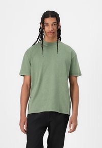 Kortärmad, rundhalsad t-shirt i olivgrön bomull. Har en avslappnad passform med en mjuk textur och synliga sömdetaljer.