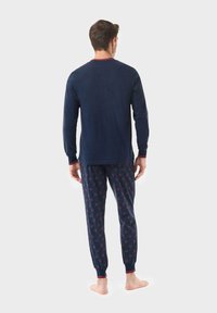 Camisa de pijama de manga larga en color navy con ribete rojo, combinada con pantalones de patrón que presentan pequeños acentos rojos sobre un fondo oscuro. Material de algodón.