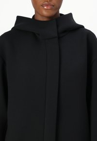 Black hooded coat with a minimalist design, featuring a smooth, wool-like texture and subtle front closure.