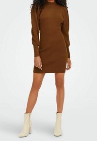 Robe en maille côtelée marron avec col montant et manches longues bouffantes, coupe ajustée, associée à des bottines blanches à la cheville. Design minimaliste.