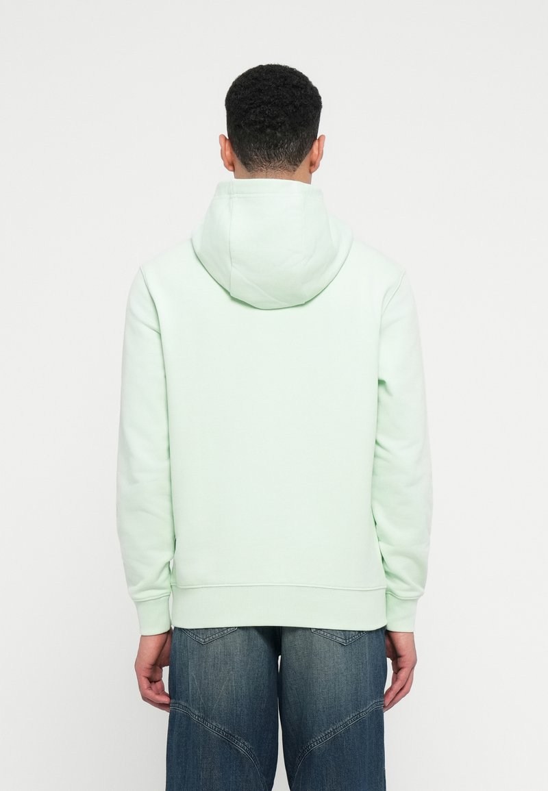 Mintgroene hoodie van zacht materiaal, met een trekkoordcapuchon en geribbelde manchetten, gecombineerd met losse, versleten donkerblauwe jeans.