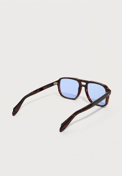 Γυαλιά ηλίου ορθογώνια με σχέδιο από χελώνια, φακοί με μπλε απόχρωση, ελαφρώς γωνιακά πλαίσια και διπλή γέφυρα σε λευκό φόντο.