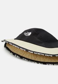 Cappello a secchiello nero e beige con un ampio ala, con il logo "THE NORTH FACE" in bianco e una fascia a contrasto lungo il bordo.