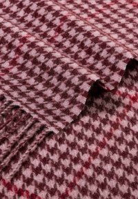 Textile featuring a houndstooth pattern in shades of burgundy and pink, with a soft wool texture and frayed edges.