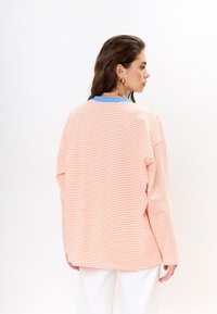 Gestreiftes weites T-Shirt in Orange und Weiß mit einem blauen Kragen. Weiche Baumwolltextur mit langen Ärmeln und lockerer Passform.