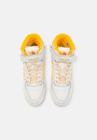 High-top sneakers in white leather with yellow accents, padded collar, perforated toe box, and a velcro strap across the ankle.