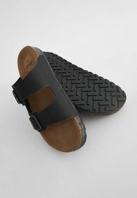 Sandalo nero con due cinturini regolabili, soletta in suede marrone, suola esterna in gomma nera testurizzata e intersuola in sughero.