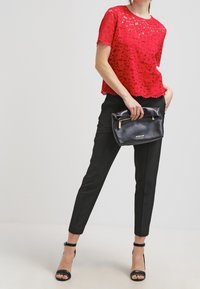 Top corto a maniche corte in pizzo rosso abbinato a pantaloni neri a sigaretta. Clutch in pelle nera con dettaglio della cerniera dorata. Tacchi neri con cinturini.