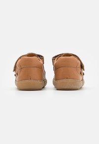 Brown leather shoes with a rounded shape, velcro straps, and a textured rubber sole. Visible stitching detail and additional padding at the heel.