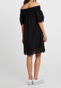 Černé šaty bez ramínek s nařaseným výstřihem, krátkými vyp puff rukávy a zvlněným lemem s výřezy. Nosené s bílými teniskami.