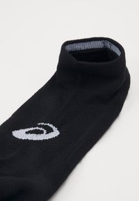 Schwarze Socke mit einem hohen gerippten Bündchen, das ein weißes Logo an der Seite und einen hellgrauen Akzent entlang der oberen Kante aufweist. Strukturierter Strickstoff.