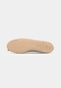 Platt skosula med en slät beige gummibotten, som har en subtil logodesign och en rundad tå. Mjukt grått övre material.