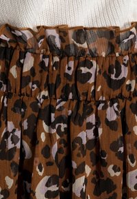 Valkoinen hame, jossa on ruskea pohja mustilla ja laventelin värisillä leopardikuvioilla. Läpinäkyvä vyötärö, jossa on röyhelöinen yläreuna. Kevyt kangas.