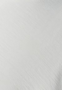 Tissu blanc texturé avec une apparence douce et légèrement froissée ; couleur uniforme sans motifs ni ornements visibles.