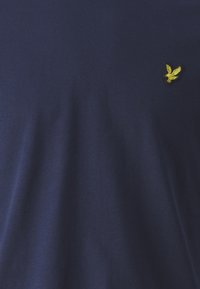 Navy blauwe katoenen t-shirt met een klein geel geborduurd vogellogo op de linkerkant van de borst. Zachte textuur met een gladde, egale afwerking.