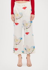 Pantalons à jambes larges en tissu blanc avec un imprimé floral, présentant de grandes fleurs blanches et rouges avec des tiges vertes et des accents bleus, taille ajustée.