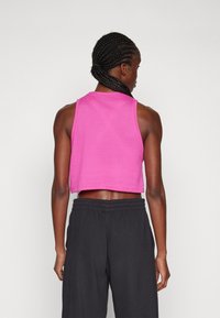Tailliertes, kurzes Tanktop in lebhaftem Pink aus Baumwolle. Glatte Textur mit weiten Armausschnitten. Kombiniert mit schwarzen, lockeren Hosen.