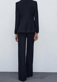 Traje ajustado azul marino que presenta un blazer entallado con hombros estructurados y pantalones de pierna ancha, confeccionado en una tela suave con líneas limpias.