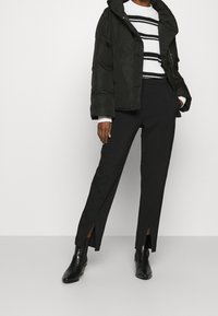 Svart puffjacka, vit tröja med svarta ränder, svarta byxor med sidospjäll och glänsande svarta ankelstövlar. Släta texturer överallt.