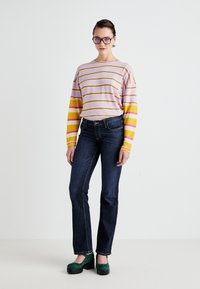 Striped sweater in pink, yellow, and white; blue straight-leg jeans; green platform shoes; model stands on a plain background.