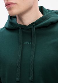 Ciemnozielona bluza z kapturem wykonana z bawełny o gładkiej teksturze. Posiada sznurki oraz subtelne logo "HUGO" na piersi.