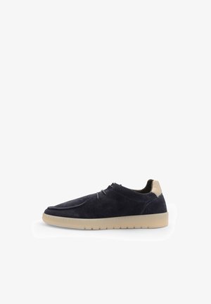 Sneaker din suede albastru navy cu detaliu pe călcâi bej, vârf rotund, șireturi minime și talpă din cauciuc texturat. Design simplu cu o finisare netedă.