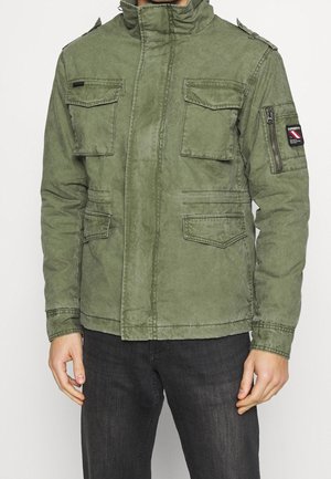 Veste de style militaire vert olive avec un col montant, plusieurs poches à l'avant et une poche zippée sur la manche. Tissu texturé, coupe décontractée.