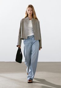 Gray linen cropped jacket with a round collar, white fitted top, light blue baggy jeans, and black tote bag, worn with flat sandals.