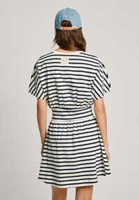 Juostuota suknelė tamsiai mėlynos ir baltos spalvų su trumpomis rankovėmis, elastinga juosmens linija ir išsiplėtusi sijono dalis. Ant nugarinės kaklo linijos yra maža etiketė.