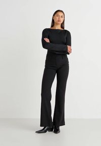 Black long-sleeve top with a crew neckline, paired with fitted black flared pants, worn with pointed black ankle boots.