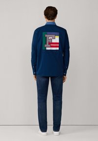 Camicia navy con design a bottoni, caratterizzata da un grande patch ricamato multicolore sulla schiena con la lettera "F" e la parola "FACONNABLE."