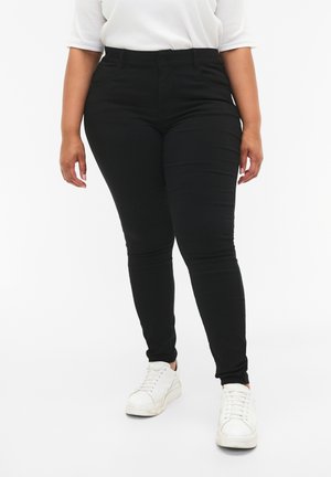 Black skinny jeans with a mid-rise waist, five-pocket design, and a smooth, stretchy fabric. Paired with white sneakers.