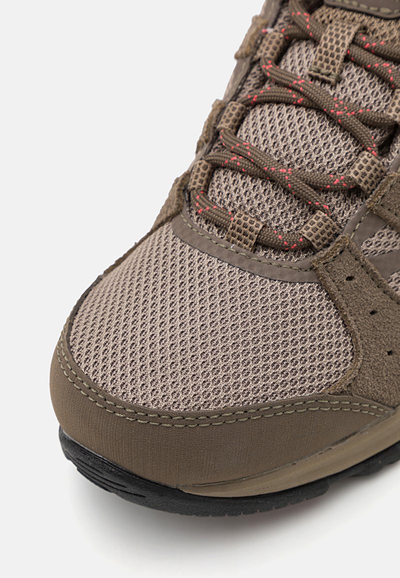 Zapatillas deportivas con parte superior de malla marrón con refuerzo, acentos texturizados y detalles rojos, complementadas por una suela de goma negra.