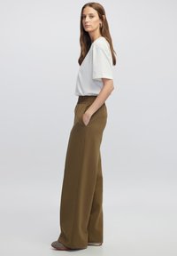 Top blanco de manga corta combinado con pantalones de tiro alto y pierna ancha de color verde oliva, que cuentan con bolsillos laterales y una cinturilla texturizada.