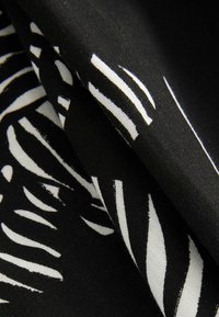 Tissu noir avec des motifs abstraits blancs en forme de feuilles, plié pour montrer la texture et les détails de l'impression et du matériau.