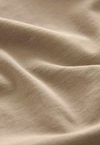 Beige látka s hladkým povrchem, zdobená jemnými žebrovanými vzory a subtilními záhyby, které ukazují měkký, lehký materiál.