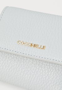 Portafoglio in pelle testurizzata blu chiaro con logo "COCCINELLE" in oro a caldo, caratterizzato da una grana distintiva e cuciture bianche.