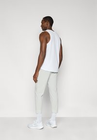 Άσπρο αμάνικο τοπ με στρογγυλή λαιμόκοψη, σε συνδυασμό με ανοιχτό γκρι cropped παντελόνια και άσπρα αθλητικά παπούτσια. Απλός σχεδιασμός και ομαλή υφή.