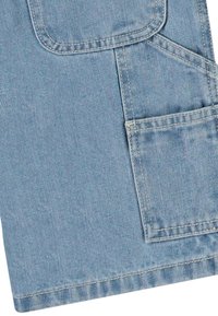 Lyseblå denimstoff med en stor lomme, mindre sidelomme, strukturert design og synlige sømdetaljer.
