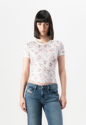 Woman with straight dark hair wears a white fitted T-shirt with multiple cat faces and blue jeans, standing against a plain white background.