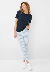 T-shirt navy à manches courtes associé à un pantalon à rayures bleu clair et blanc à coupe ample, complété par des baskets blanches.