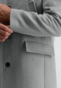 Grijs wollen jasje met een gladde textuur, voorzien van een knoopsluiting aan de voorkant, een buitenzak en een opgerolde mouw.