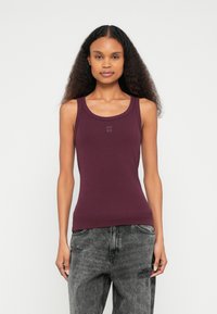 Viininpunainen hihaton toppi pehmeästä kankaasta, pyöreällä pääntiellä ja hillityllä "HUGO"-logolla rinnassa. Yhdistetty harmaisiin kulutuksiin revittyihin farkkuihin.