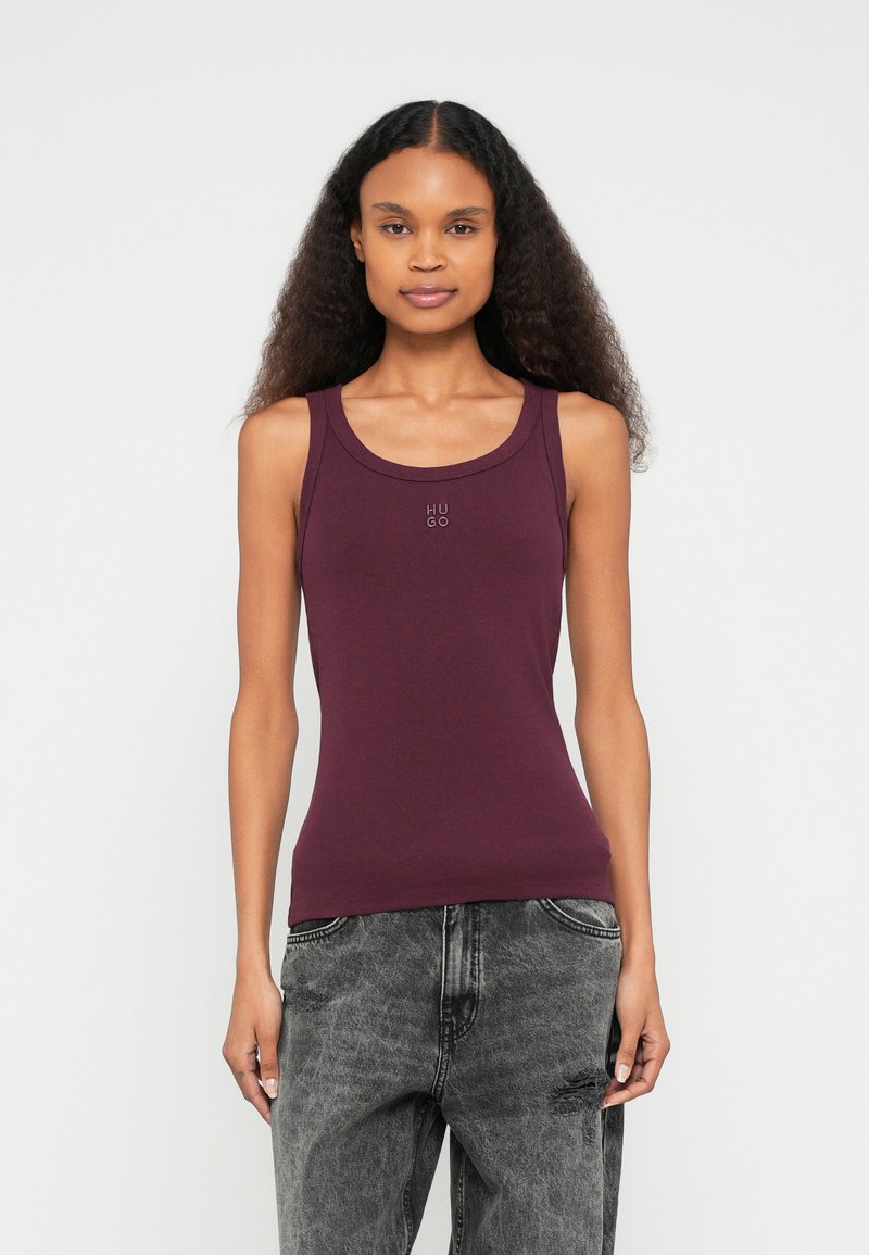 Viininpunainen hihaton toppi pehmeästä kankaasta, pyöreällä pääntiellä ja hillityllä "HUGO"-logolla rinnassa. Yhdistetty harmaisiin kulutuksiin revittyihin farkkuihin.