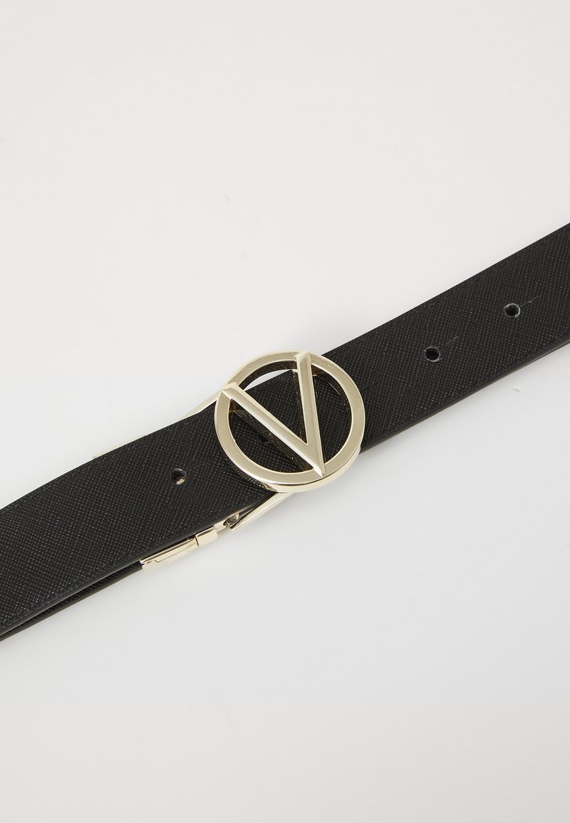 Ceinture en tissu noir avec une boucle ronde en or au design en V. La ceinture possède plusieurs trous pour ajuster la taille et a une texture lisse.
